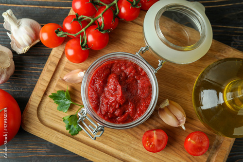 Jar with tomato paste on wooden table with ingredients