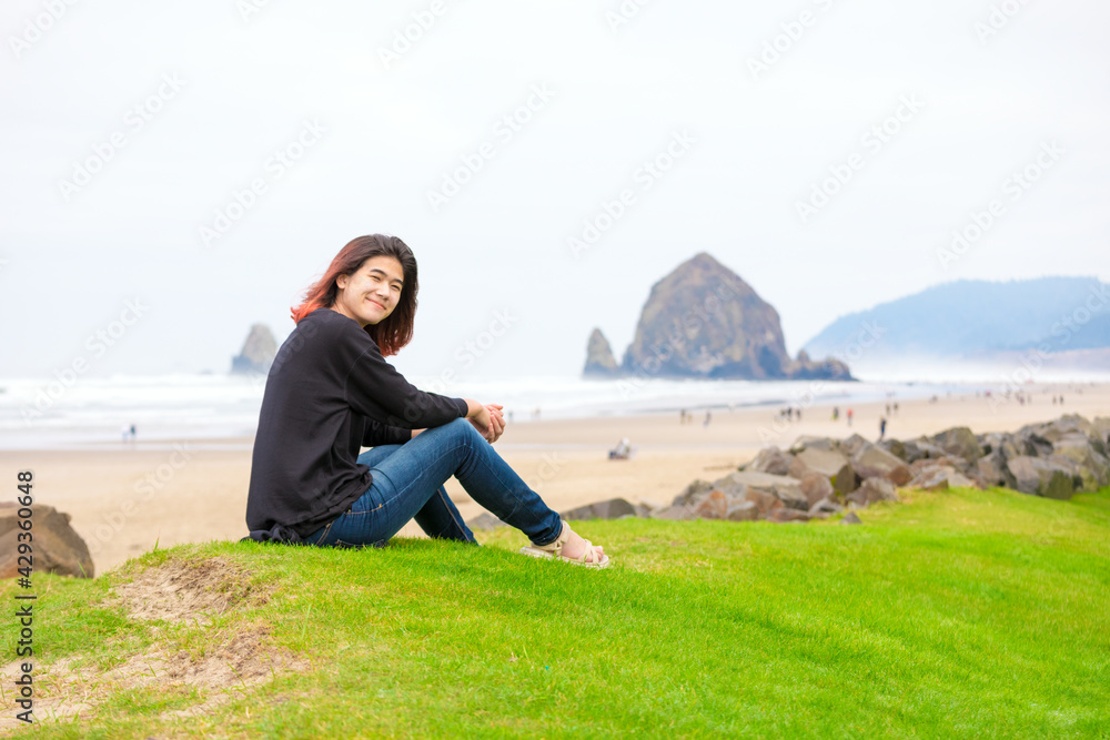 Biracial teen girl sitting near ocean in Pacific Northwest