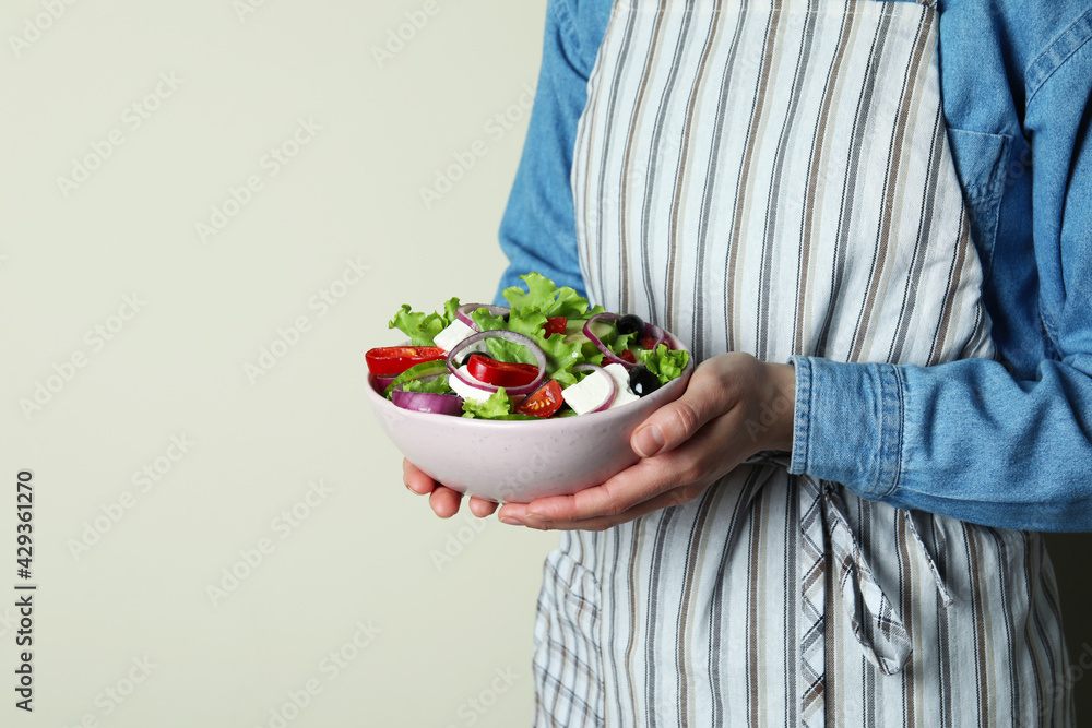 Woman in apron holds bowl of greek salad Woman in apron holds bowl of greek salad