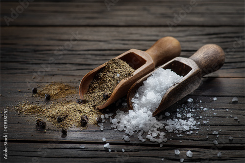 Sea salt and ground pepper in the wooden spoons on old wooden background. Two most popular ingredients that you put into food.