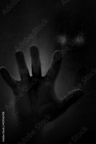 Horror scene of a man with hand against wet shower glass. Black and white image. Horror concept. Vertical image