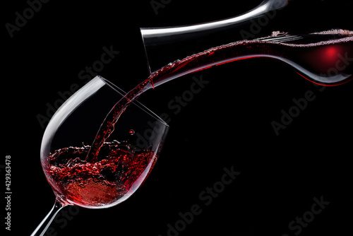 Red wine is poured into a wine glass on a black background.