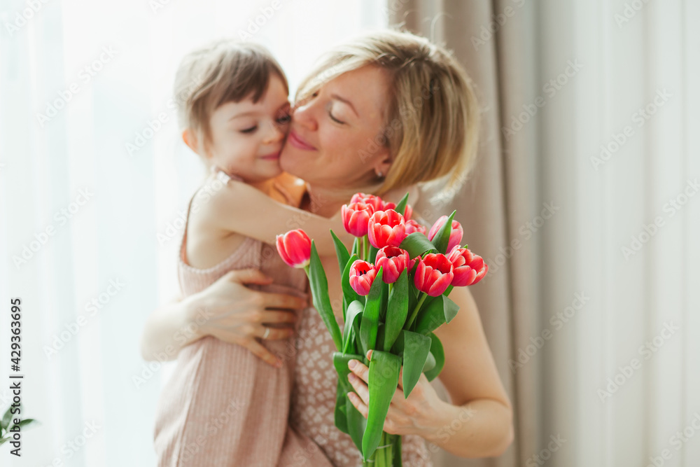 Little girl hugging her mother holding tulips Little girl hugging her mother holding tulips