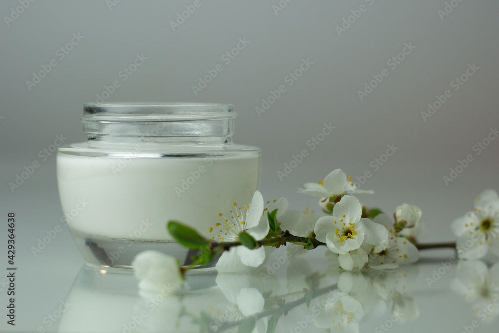 Closeup of a jar of moisturizer and blooming flowers. Concept of spring skincare. Closeup of a jar of moisturizer and blooming flowers. Concept of spring skincare.