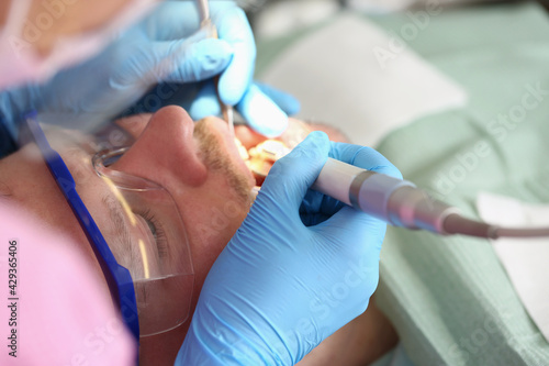 Dentist doctor treating teeth of young man in clinic closeup