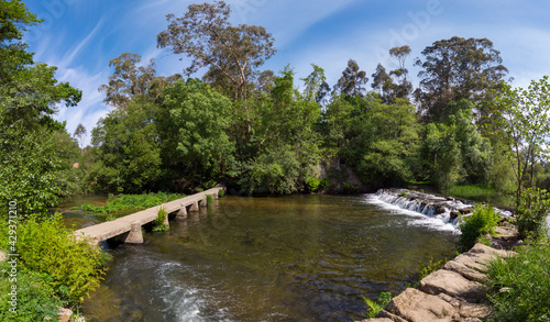 Panoramic view of a beautiful little waterfall cascade and an old stone footbridge over the Neiva River in Antas, Esposende, Portugal.