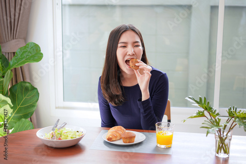 Young asian woman eating bread with a glass of fresh orange juice and healthy salad while breakfast