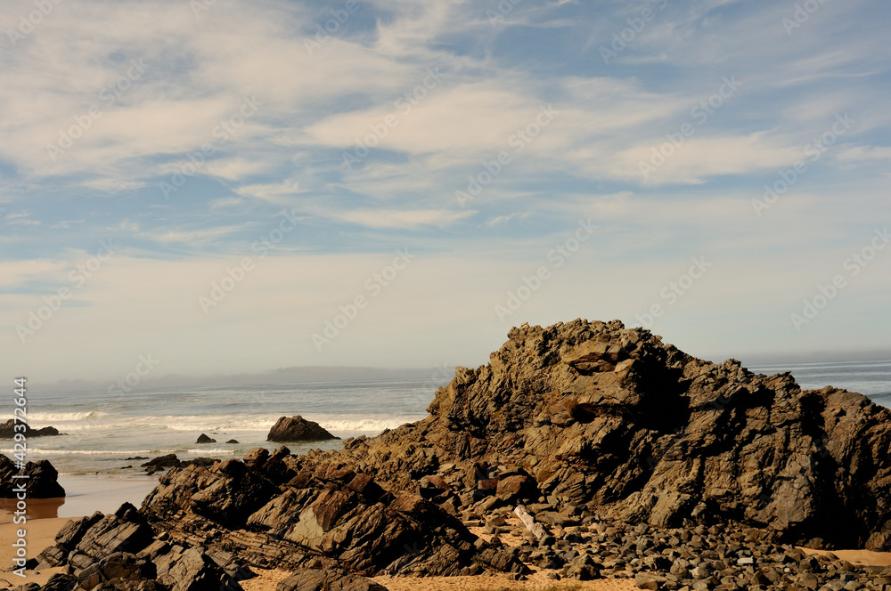 A contrast of rough and rugged rocks against soft clouds and blue sky at Keurbooms on the Garden Route, Western Cape A contrast of rough and rugged rocks against soft clouds and blue sky at Keurbooms on the Garden Route, Western Cape