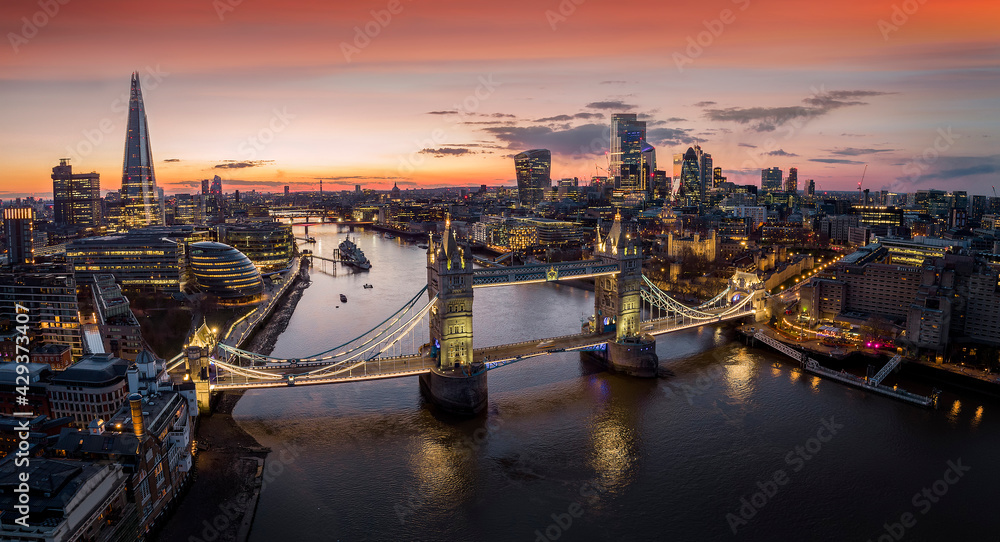 Panoramic, aerial view to the cityscape of London with Tower Bridge and the illuminated skyscrapers of the city during dusk, United Kingdom