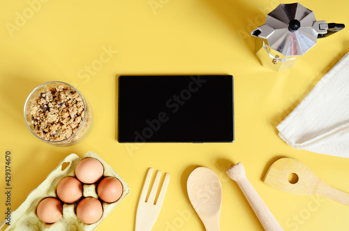 Flat lay with tablet with black mockup and place for text on yellow background. Food blogger's workplace. Culinary blog, recipe template, online cooking courses. Healthy food concept. Copy space.