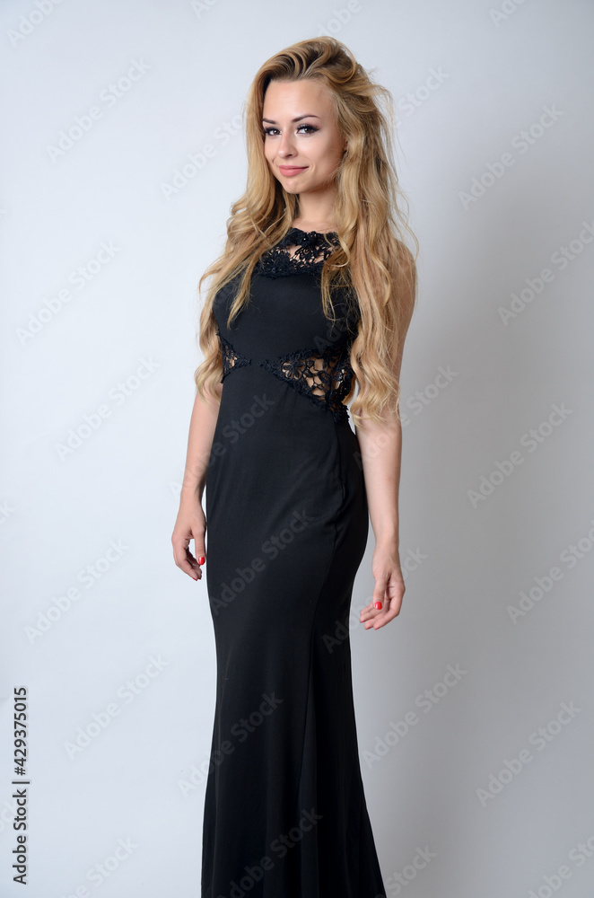 Model from Poland posing with long, black dress. Charming young woman posing in studio with white background. Model from Poland posing with long, black dress. Charming young woman posing in studio with white background.