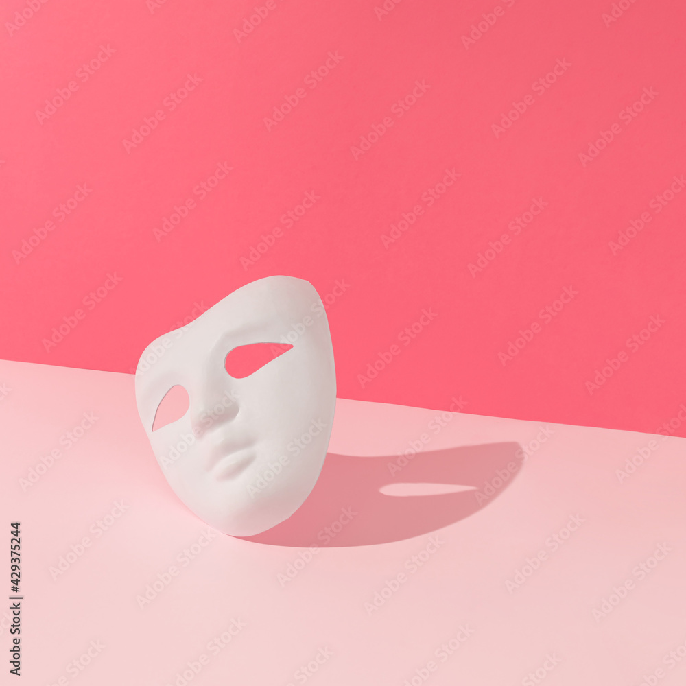 White costume ball face mask with sunlight shadow on bright pink background. Minimal abstract concept. White costume ball face mask with sunlight shadow on bright pink background. Minimal abstract concept.