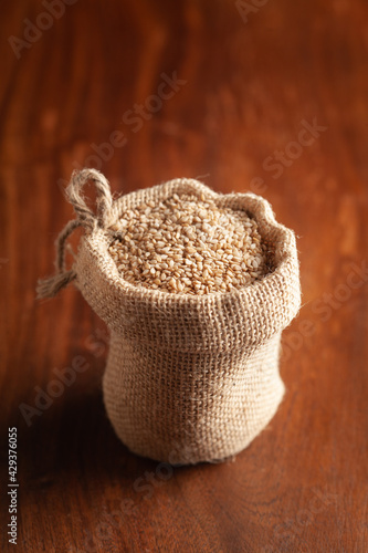 Close-up of Organic White Sesame seeds(Sesamum indicum) or white Til with shell in a standing jute bag over wooden brown background.