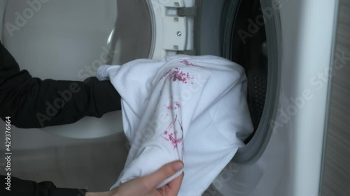 A woman sprinkles a soiled t-shirt with laundry detergent before washing it in the washing machine. Preparing dirty white t-shirt to laundry, hands closeup. She is putting t-shirt in washing machine.