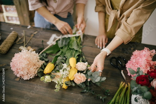 Bild auf Leinwand Two young women florist working in flower studio, making beautiful bouquet using fresh plants and flowers