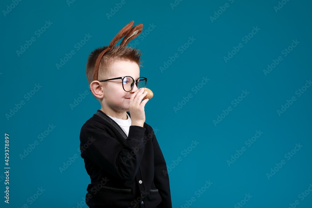 Cheerful boy in rabbit bunny ears on head on blue studio background. Excited crazy smiling happy child in glasses. Easter blue color of the year painting eggs in hands. Easter and holidays. Cheerful boy in rabbit bunny ears on head on blue studio background. Excited crazy smiling happy child in glasses. Easter blue color of the year painting eggs in hands. Easter and holidays.