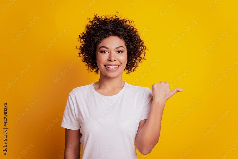 Portrait of young woman indicate thumb empty space on yellow wall Portrait of young woman indicate thumb empty space on yellow wall
