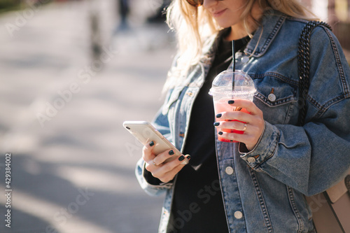 Pretty prengant woman dringking strawberry lemonade while walking outdoors. Portrair of attractive female in sunglasses using phone photo