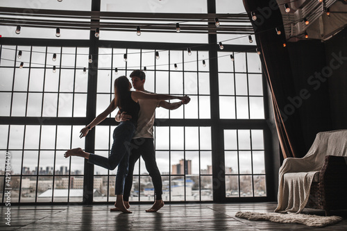 a girl and a guy dance against the background of a huge window  the silhouette of a dancing couple