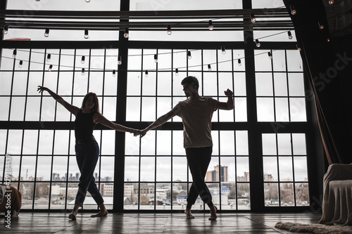 a girl and a guy dance against the background of a huge window, the silhouette of a dancing couple