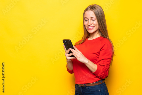Young woman chatting by mobile phone isolated over yellow wall background.
