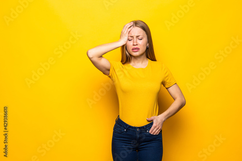 Young woman forgetting something, slapping forehead with palm and closing eyes isolated on a yellow background