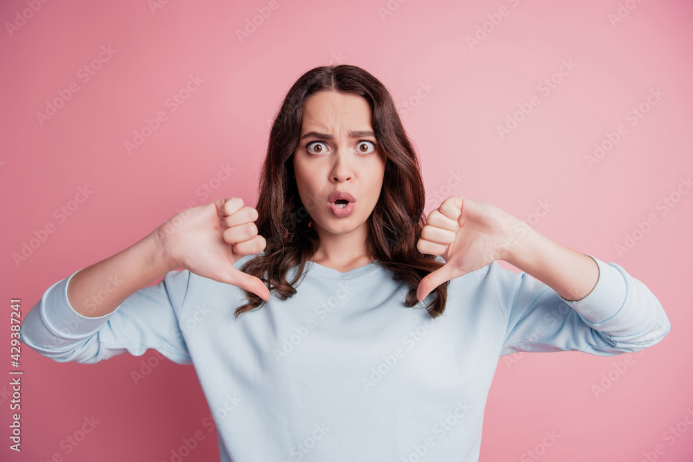 Young shocked stunned brunette girl showing two thumbs down open mouth on pink wall Young shocked stunned brunette girl showing two thumbs down open mouth on pink wall