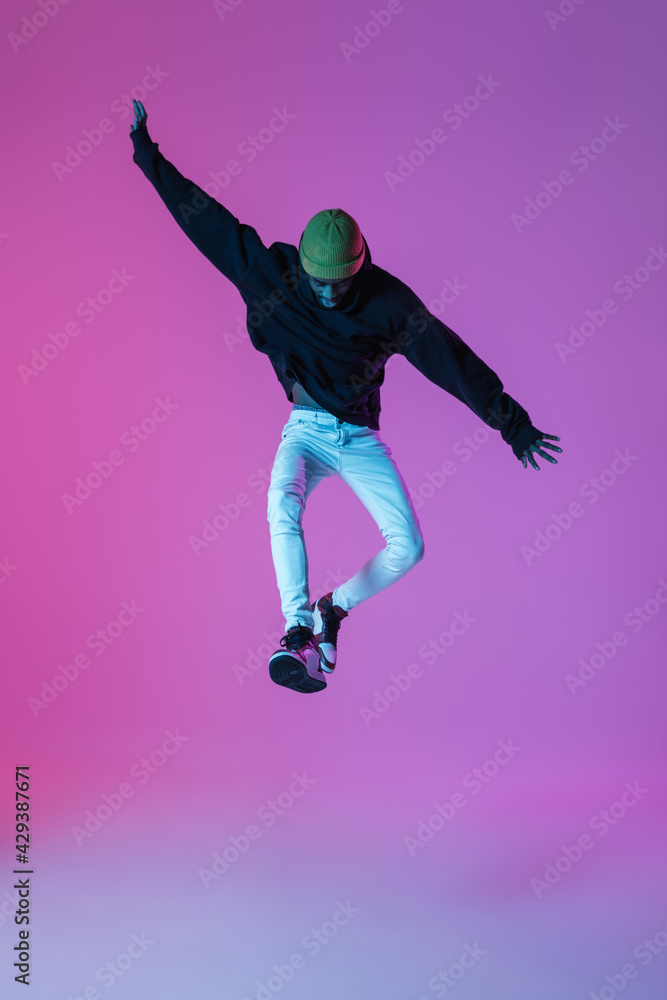 Young stylish man in modern street style outfit isolated on gradient background in neon light. African-american fashionable model in look book, musician performing.