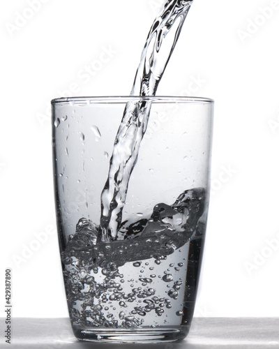 Glass of water being filled. Close up pouring clear water in transparent drinking glass over white background © Julian