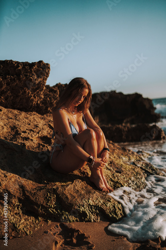 Chica guapa morena española en el sur de españa en una cala natural con piedras y olas salvajes disfrutando de un atardecer calido de verano 