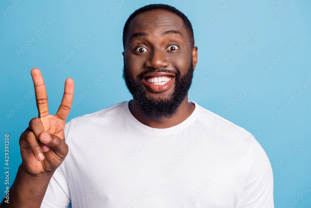 Photo of friendly guy toothy beaming smile show v-sign on blue background Photo of friendly guy toothy beaming smile show v-sign on blue background