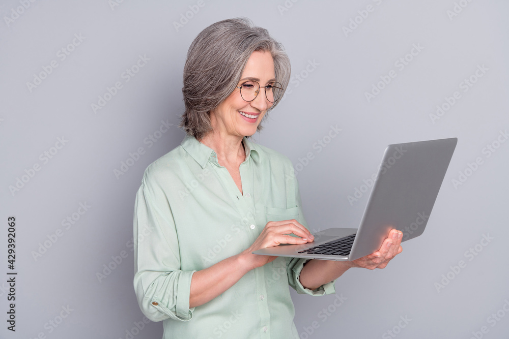 Photo of happy cheerful lovely mature businesswoman in glasses working in computer isolated on grey color background Photo of happy cheerful lovely mature businesswoman in glasses working in computer isolated on grey color background