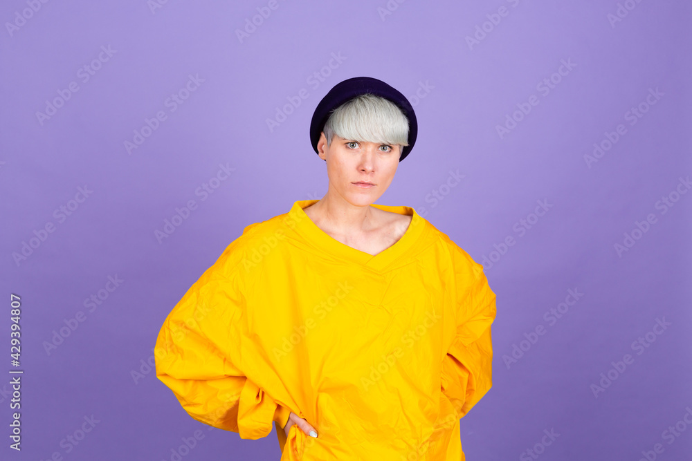 Stylish european woman on purple background posing wearing yellow large jacket and hat Stylish european woman on purple background posing wearing yellow large jacket and hat