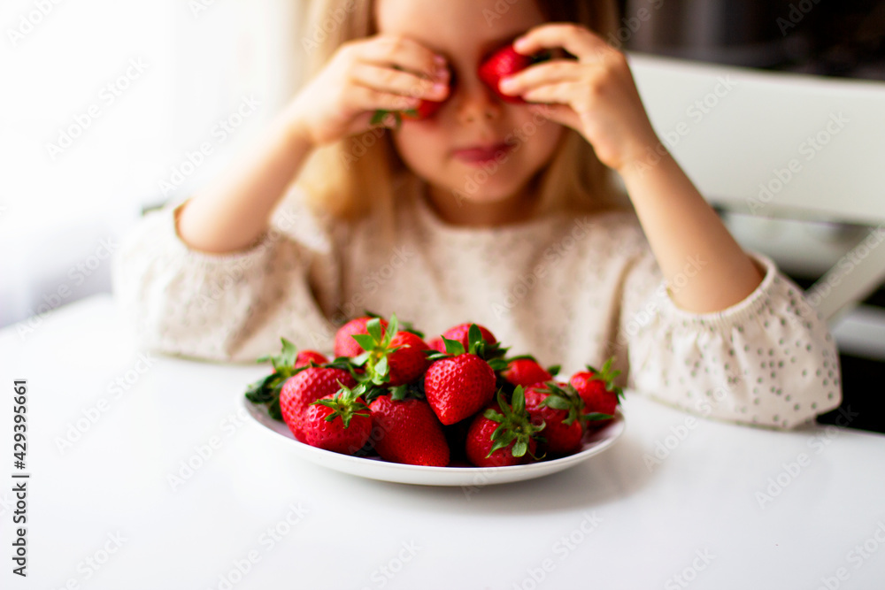 Cute little girl eating fresh strawberry in the kitchen. Healthy vitamin snack for kids. Ripe fresh berries. Harvest season. Natural vitamins . Cute little girl eating fresh strawberry in the kitchen. Healthy vitamin snack for kids. Ripe fresh berries. Harvest season. Natural vitamins .
