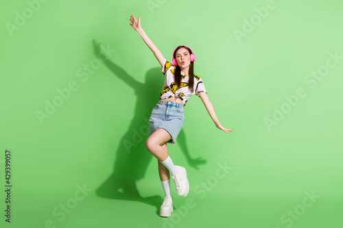 Full length photo of happy young woman dance sing good mood wear headset isolated on green color background