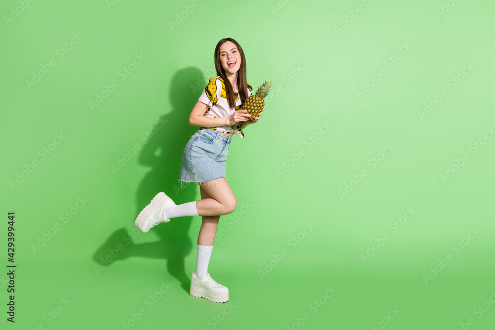 Full body photo of attractive happy young woman hold pineapple smile summer isolated on green color background Full body photo of attractive happy young woman hold pineapple smile summer isolated on green color background