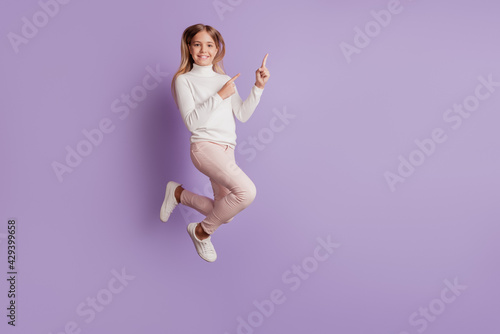 Portrait of happy little child girl jumping direct forefingers copyspace