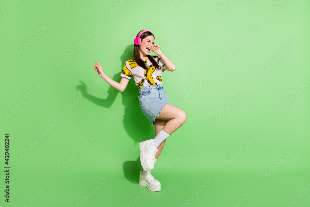 Full body photo of joyful happy cheerful girl look empty space wear headphones isolated on green color background