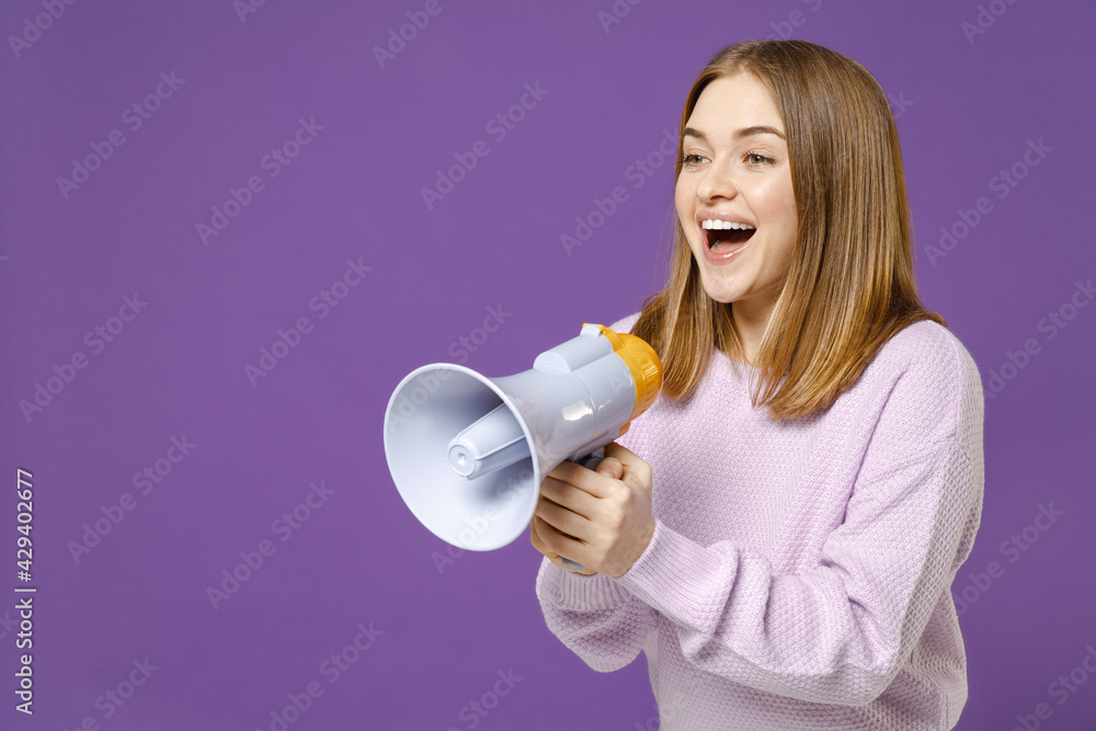 Young fun expressive happy smiling student caucasian woman 20s wear purple knitted sweater scream aside shouting in megaphone isolated on violet background studio portrait. People lifestyle concept Young fun expressive happy smiling student caucasian woman 20s wear purple knitted sweater scream aside shouting in megaphone isolated on violet background studio portrait. People lifestyle concept