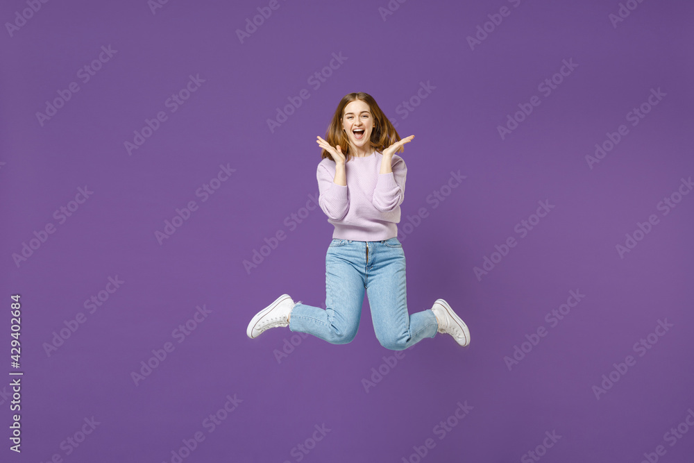 Full length young excited overjoyed happy woman 20s wearing purple knitted sweater jump high do winner gesture clench fist isolated on violet color background studio portrait People lifestyle concept.