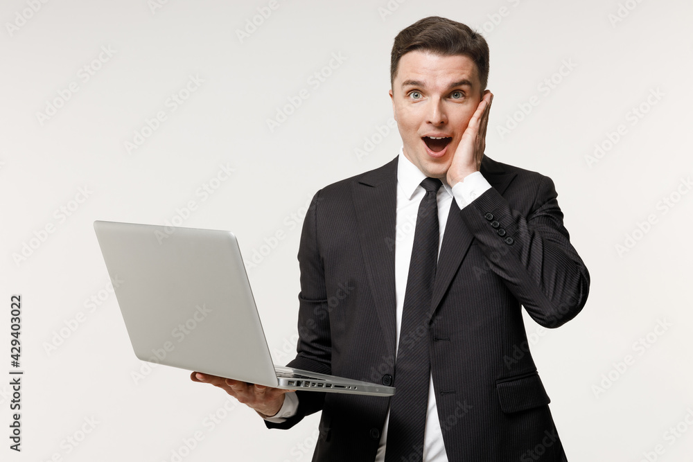 Young shocked employee business corporate lawyer man 20s wearing classic formal black grey suit shirt tie work in office hold laptop pc computer hold face isolated on white background studio portrait Young shocked employee business corporate lawyer man 20s wearing classic formal black grey suit shirt tie work in office hold laptop pc computer hold face isolated on white background studio portrait