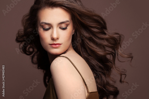 Portrait of young pretty woman brunette with dark blowing curly hair and clear healthy skin on brown background