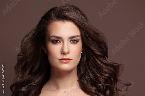 Healthy brunette woman with brown curly hair on brown background