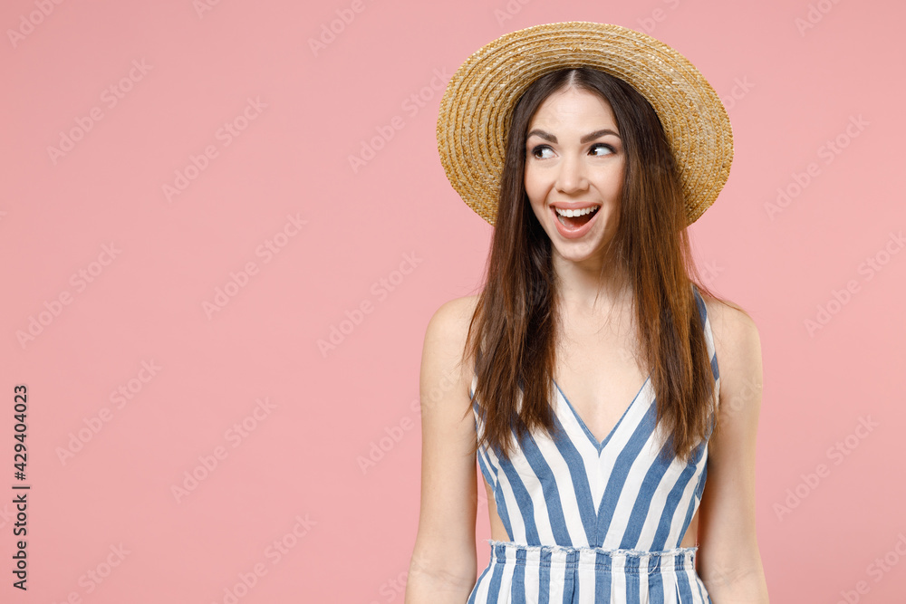 Young excited surprised happy positive cheerful caucasian woman in summer clothes striped dress straw hat looking aside isolated on pastel pink background studio portrait. People lifestyle concept Young excited surprised happy positive cheerful caucasian woman in summer clothes striped dress straw hat looking aside isolated on pastel pink background studio portrait. People lifestyle concept