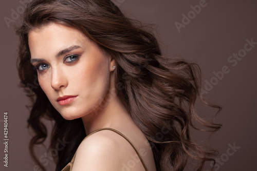 Portrait of pretty young woman with blowing healthy curly hairdo and clear skin on brown background