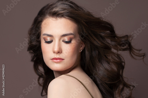 Portrait of perfect young woman with blowing long perfect dark hair and clear skin on brown background