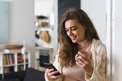 woman using mobile phone and drinking morning coffee at home