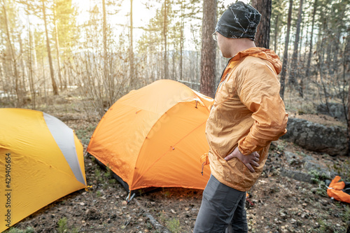 A male traveler is standing in the forest near the tents in a tent camp. Concept of hiking, spending time in nature