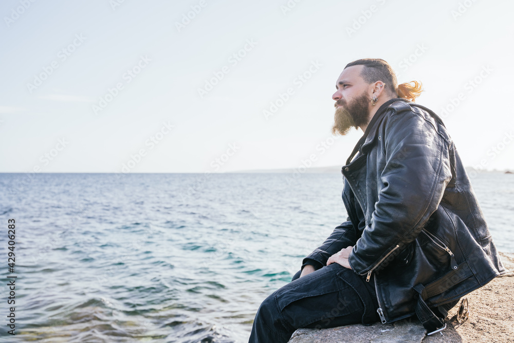 Caucasian man with long hair and beard looking at the sea seriously at sunset on a beach in Portals. Palma de Mallorca, Spain (Copyspace)