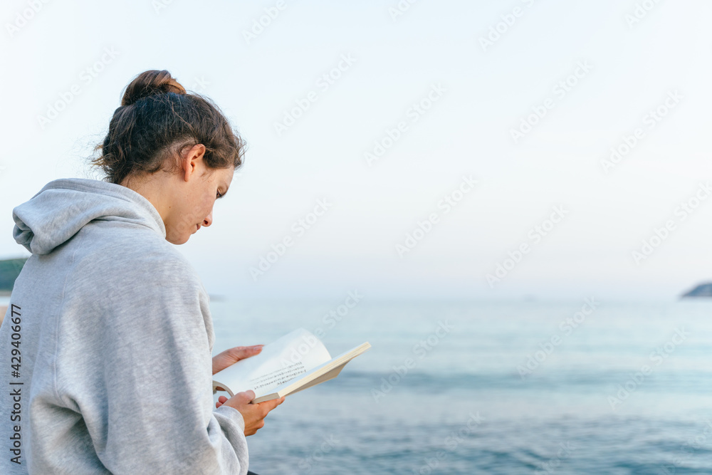 Caucasian woman reading a book on a bridge over the sea at Magaluf beach. Palma de Mallorca, Spain.